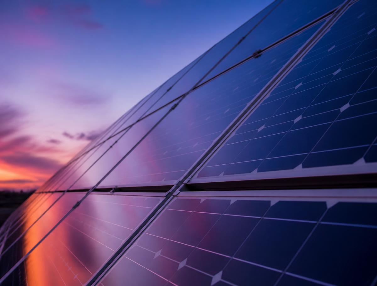 Painéis solares de uma usina fotovoltaica refletindo o céu ao anoitecer